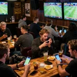 Excited patrons engaging in sports betting at 28Bet with mobile apps and live match screens.