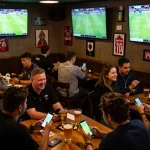 Tỷ lệ kèo nhà cái 5 displayed on sports screens while patrons cheer and place bets at a lively bar