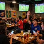 Fans celebrating ผลบอลวันนี้ scores while using betting apps at a lively sports bar
